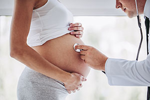 Arzt hört mit Stethoskop den Babybauch einer schwangeren Frau ab